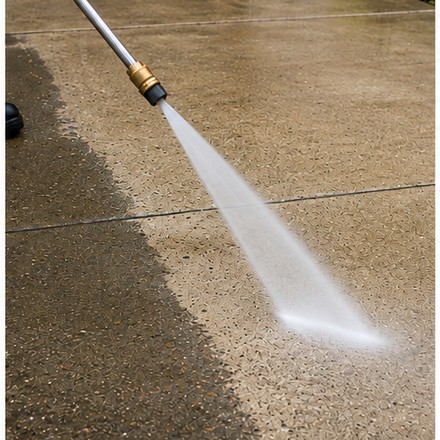 Pressure washing a driveway next to a garage